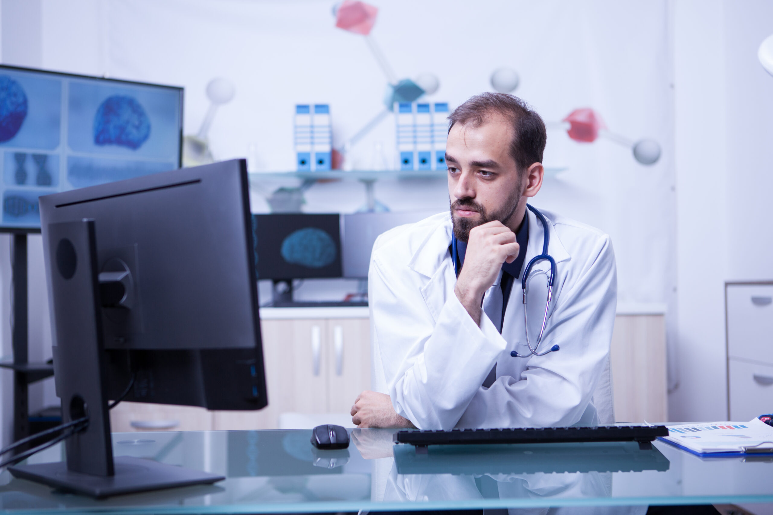 Portrait of thoughtful young doctor looking into the monitor in his cabinet
