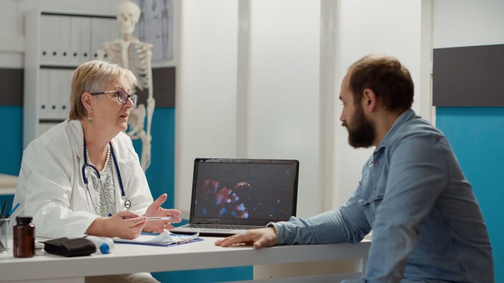 Female doctor looking at coronavirus illustration on laptop with sick patient talking about medication and prevention. Animation of virus on display to cure disease in doctor's office.